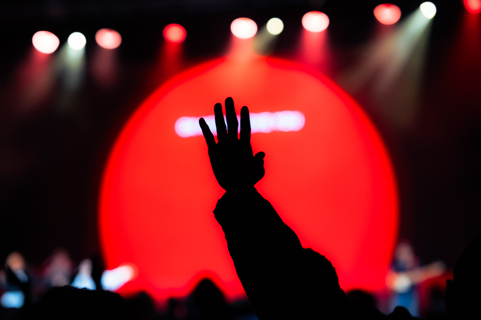 Raised hand silhouetted against blurred stage lighting at Gospel Forum Stuttgart